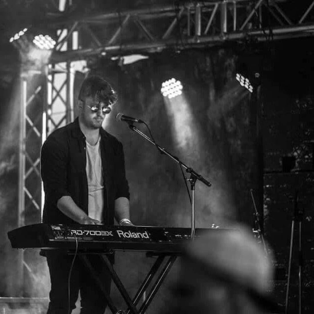 Adam Whybro playing keyboard live with the band FENDS under stage lighting, in black and white