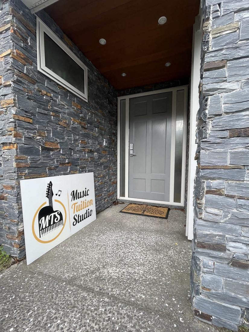The studio entrance at 24 Westerley Place, a grey front door in a schist stone wall with the Music Tuition Studio sign standing beside it