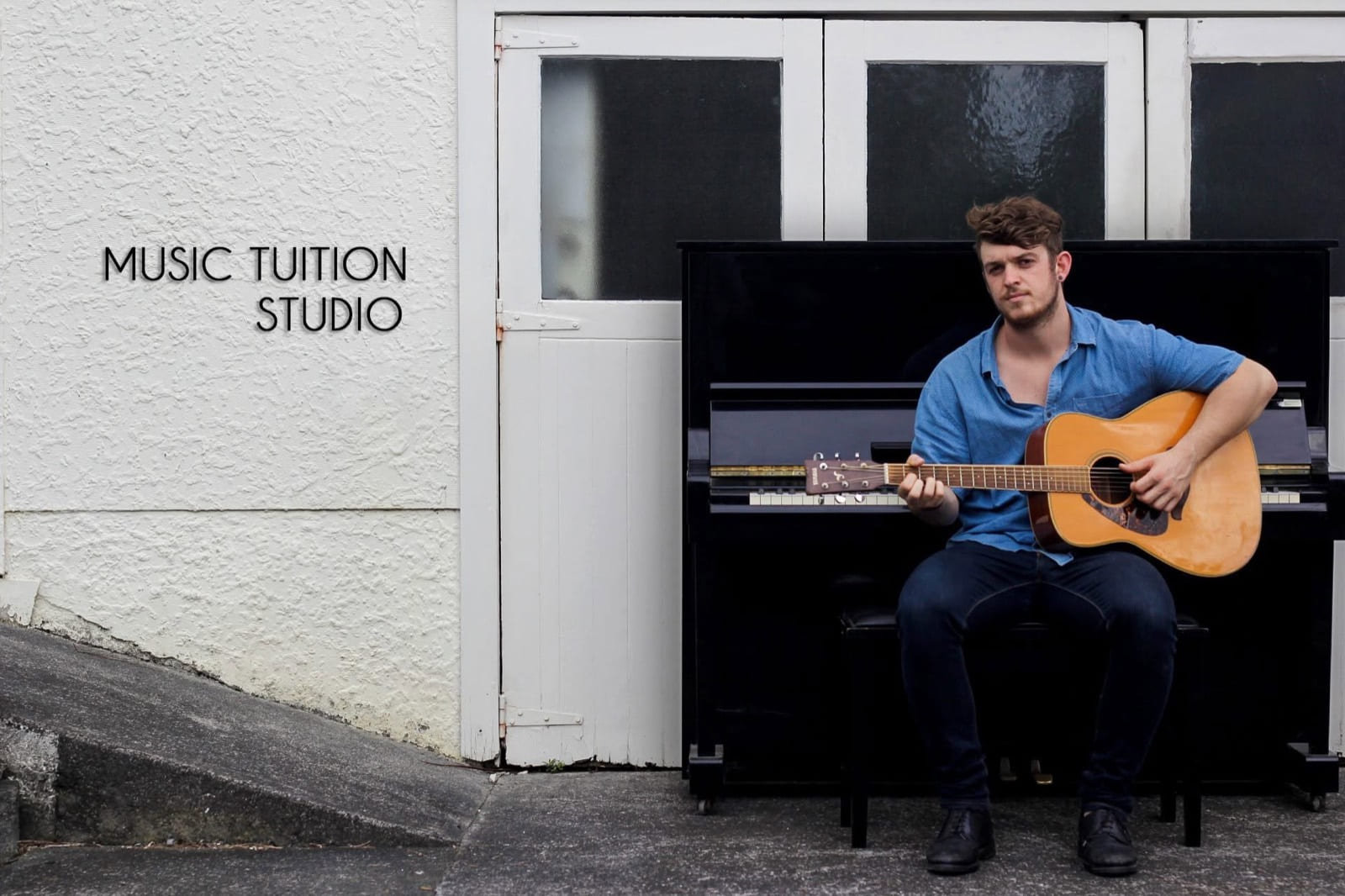 Adam with an acoustic guitar, sitting at an upright piano outside the Long Bay studio