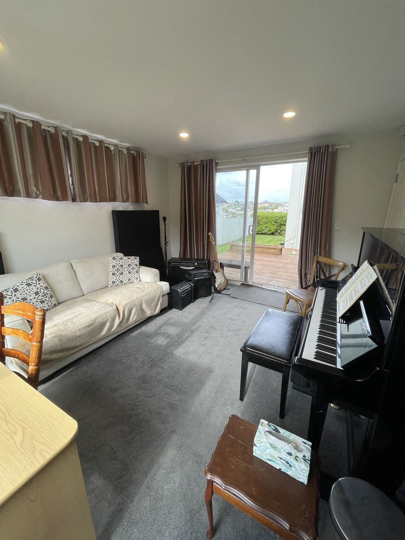 The teaching room at the Long Bay studio looking toward sliding doors onto the deck, with a sofa on the left and an upright piano on the right