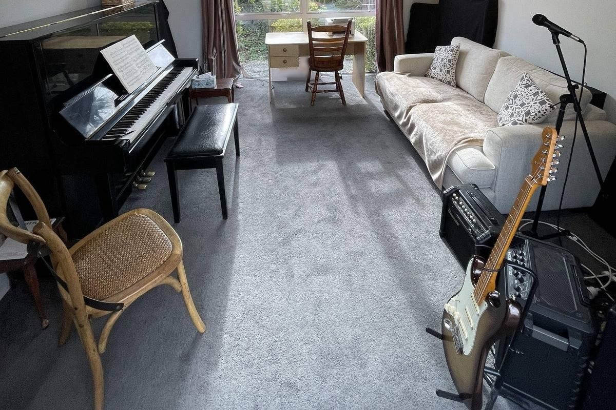 The upright piano, bench and open sheet music on the left of the Long Bay teaching room, with an electric guitar and two amplifiers in the foreground on the right